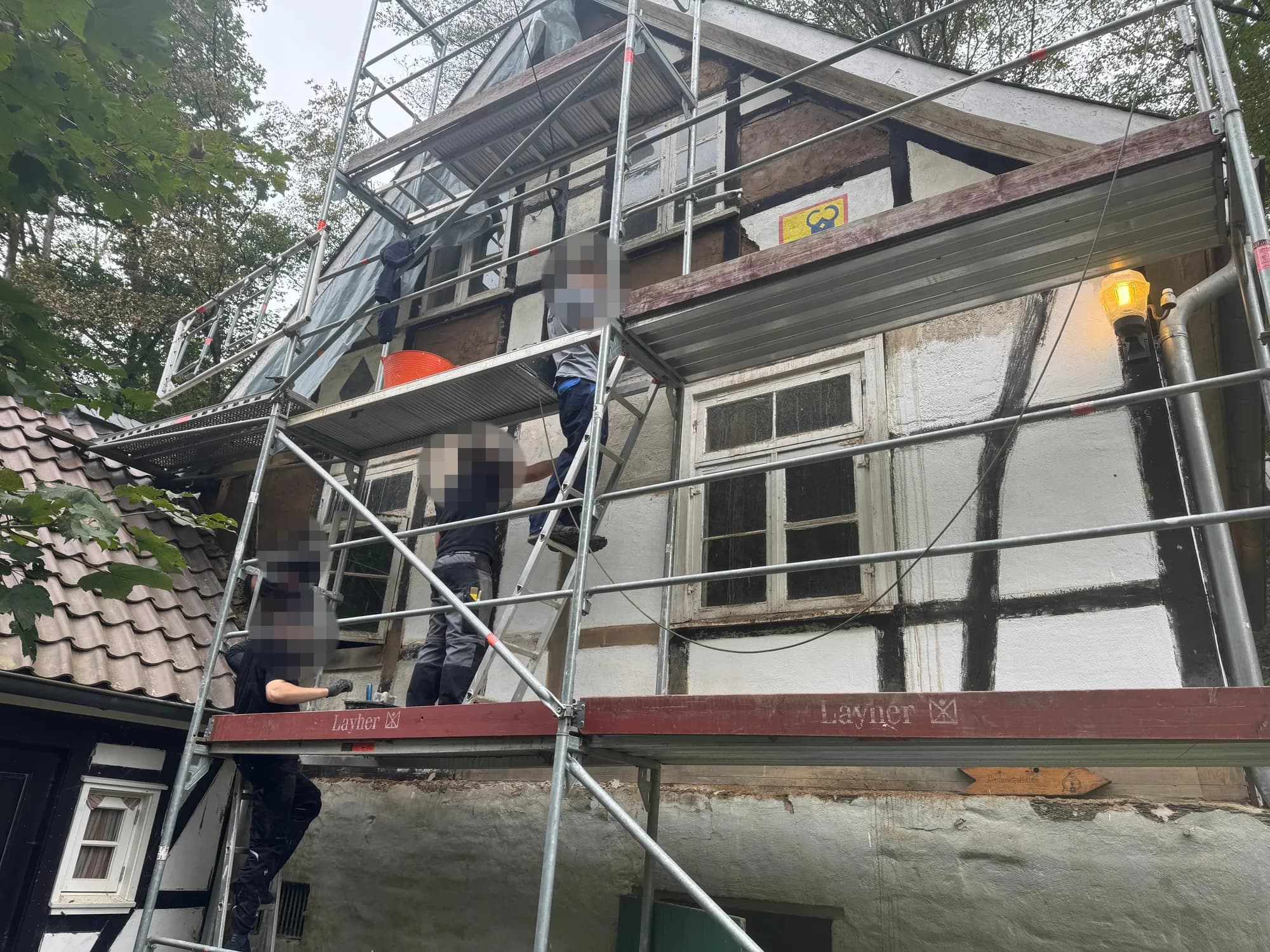 Mehrere Helfende arbeiten auf dem Gerüst und auf einer Leiter an der Fachwerkfassade.