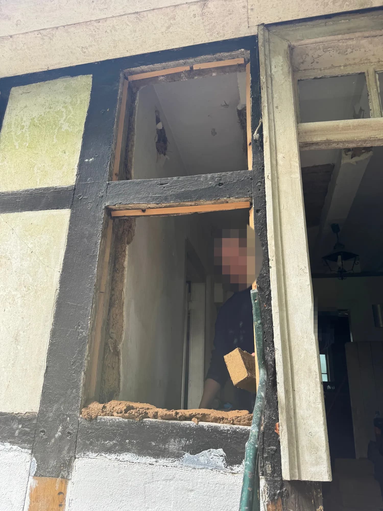 Durch ein geöffnetes Gefach reicht eine Person im Haus einen Lehmstein heraus, unten liegt frischer Lehm.